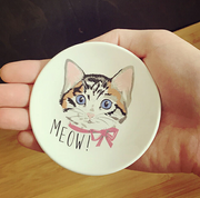 Round ceramic coaster with a cat illustration and 'MEOW!' text held in a hand.