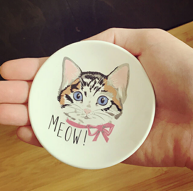 Round ceramic coaster with a cat illustration and 'MEOW!' text held in a hand.